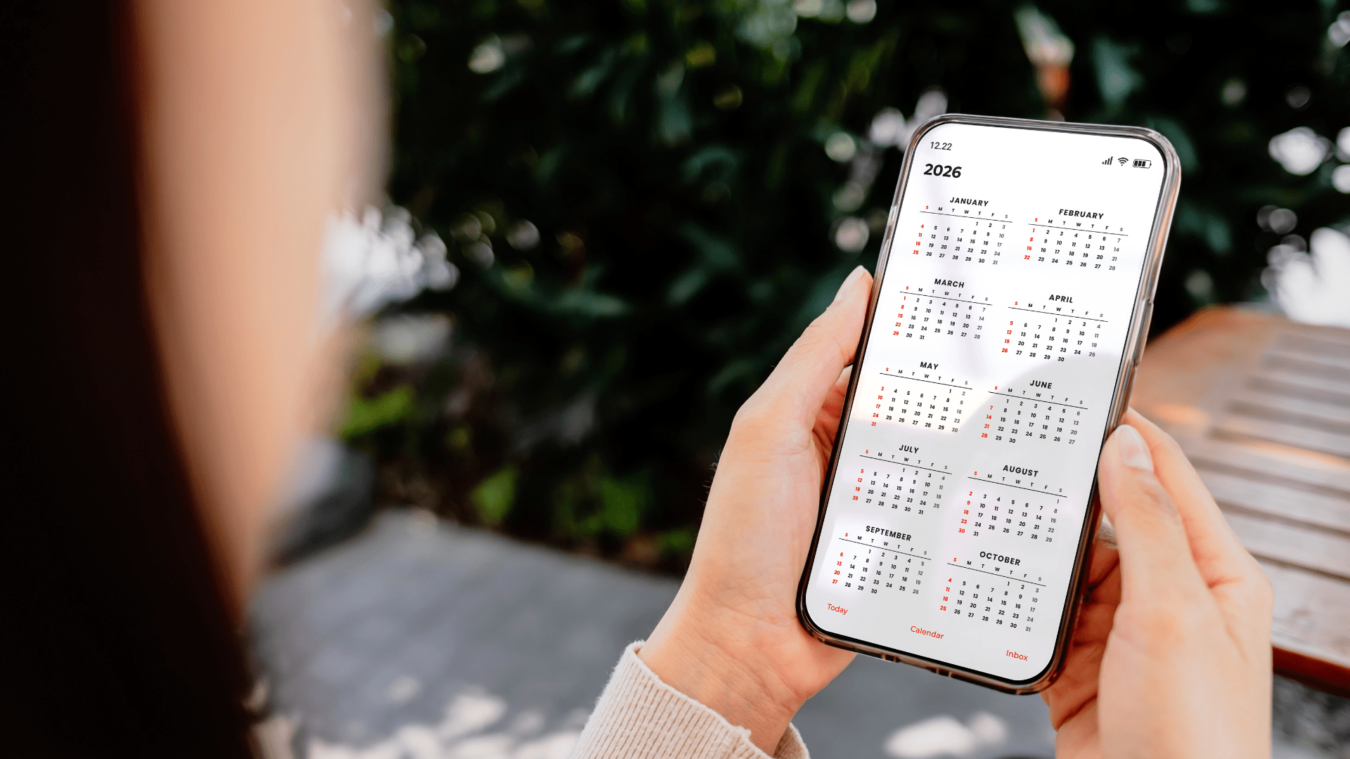 Frau hält ein Smartphone mit geöffnetem Jahreskalender 2026 in der Hand, Monate Januar bis Oktober sichtbar.