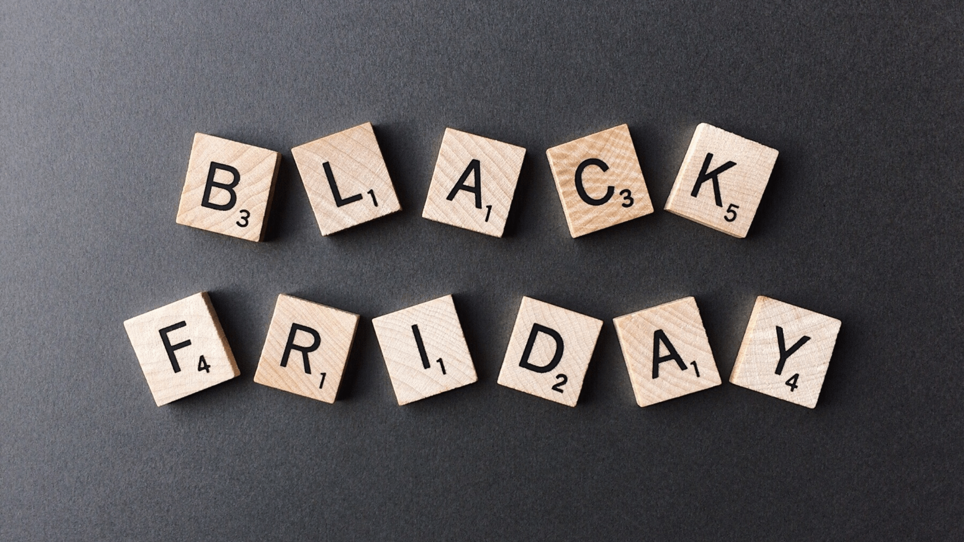 Der Schriftzug 'Black Friday' aus hellen Holz-Scrabble-Steinen auf dunkelgrauem Hintergrund.